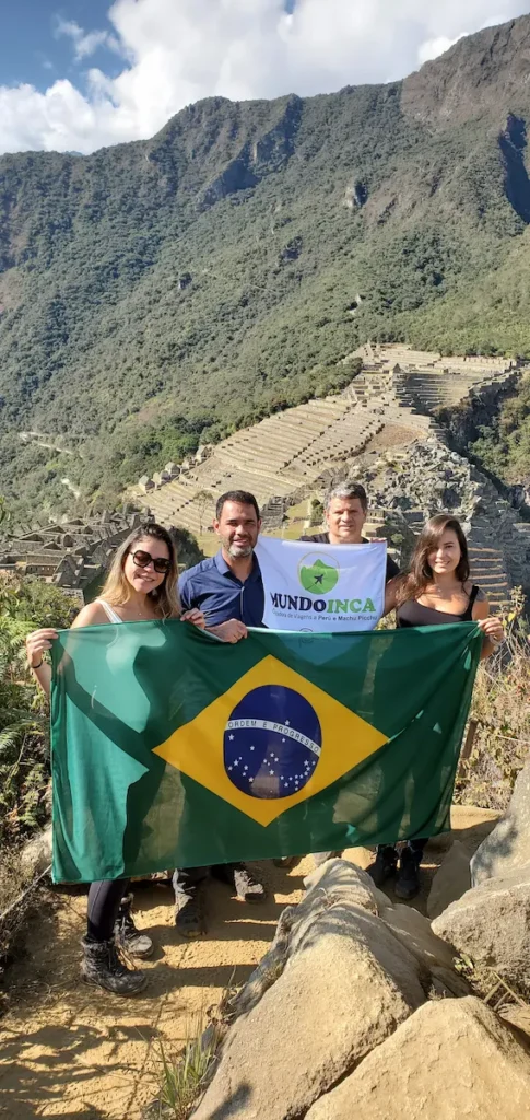 Grupo de turistas brasileños celebrando en Machu Picchu con la bandera de Brasil y el equipo de Mundo Inca.