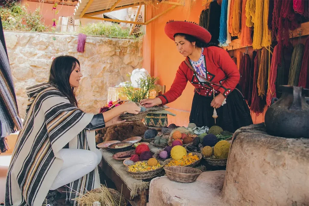 Mujer andina de Chinchero demostrando el uso de tintes naturales en la lana de alpaca a un turista.