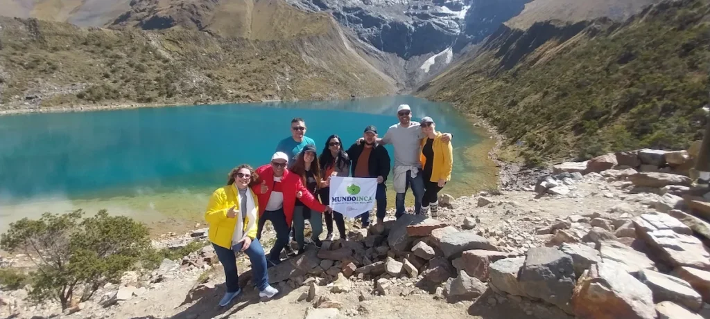 Grupo de aventureiros celebrando a chegada à Lagoa Humantay com a bandeirola da agência após a trilha.