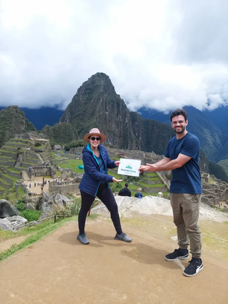 Casal segurando com orgulho a bandeirola da agência na cidadela inca de machu picchu, viagem segura para casais.