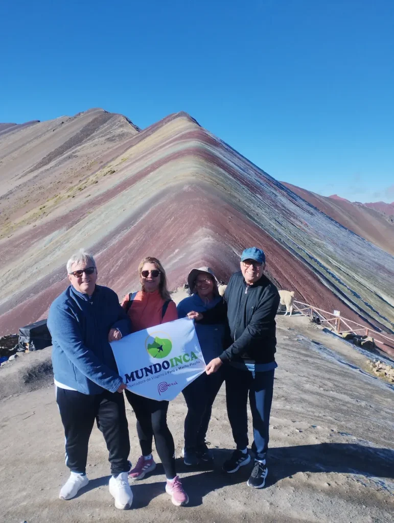 Grupo de trilheiros alcançando a meta na Montanha Vinicunca com a bandeirola da agência.